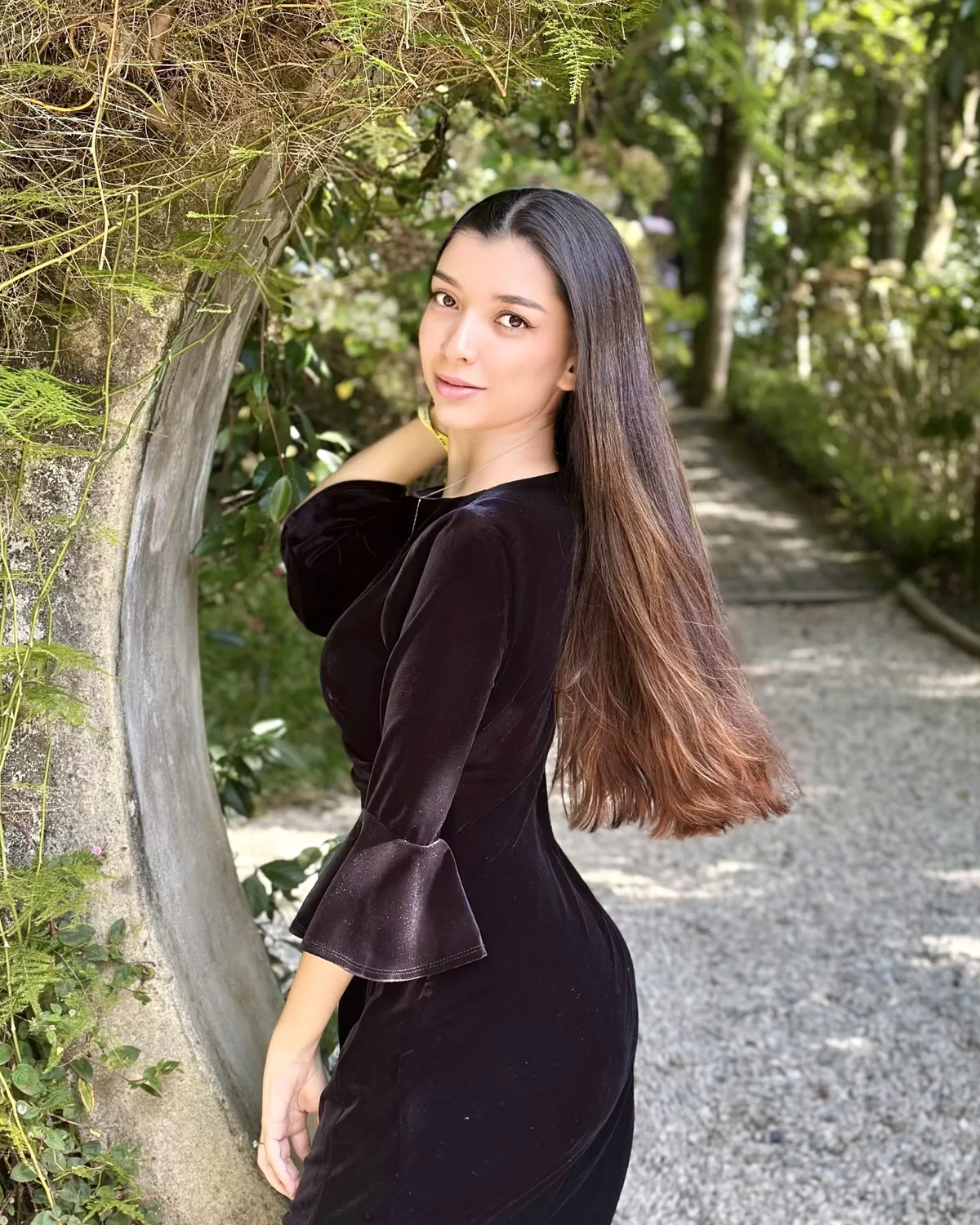 Ana Carolina em um jardim, com vestido de veludo preto, olhando por cima do ombro.